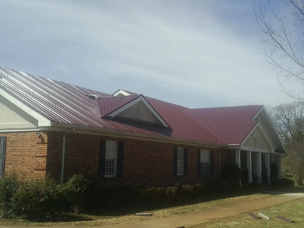 Red metal roof with gabled entries on a long brick building, from a Hail Damage Roof Repair job in Pikeville