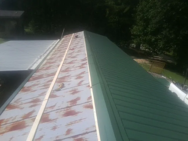 Old rusted panels beside newly installed green metal roofing — Wind Damage Roof Repair by Roofing Brothers in Pikeville