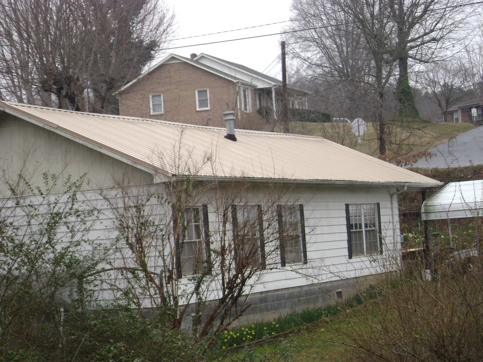 Tan metal roof on a white sided house set into a hillside — Commercial Roofing by Roofing Brothers in Pikeville